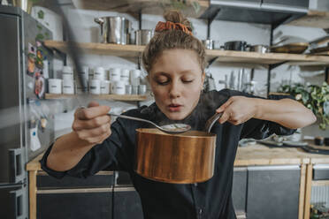 Junge weibliche Köchin, die in der Küche stehend die Brühe der Suppe probiert - MFF07055