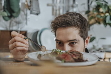 Chef concentrating while garnishing tomahawk steak with vegetable in kitchen - MFF07067