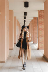 Young woman with reusable coffee cup walking through corridor - FMOF01345