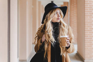 Frau mit Hut hält Kaffeetasse und schaut weg - FMOF01348