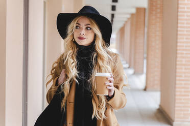 Frau mit langen Haaren hält Kaffeetasse und schaut weg - FMOF01349