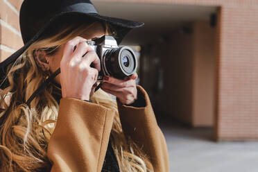 Young woman in hat filming through camera during sunny day - FMOF01359