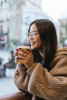 Lächelnde junge Frau schaut durch das Fenster, während sie in einem Café Kaffee trinkt - JRVF00218
