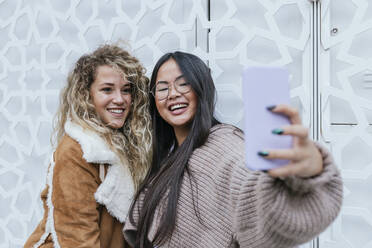 Beautiful female friends taking selfie through smart phone while standing against metal gate - JRVF00222