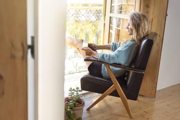 Frau mit digitalem Tablet, die zu Hause auf einem Sessel sitzt - SBOF02624