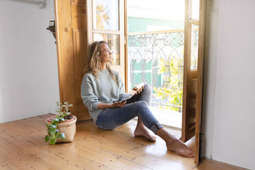 Nachdenkliche Frau mit digitalem Tablet und Blick aus dem Fenster zu Hause - SBOF02631