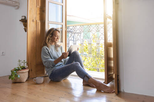 Frau benutzt digitales Tablet, während sie zu Hause auf dem Boden sitzt - SBOF02633