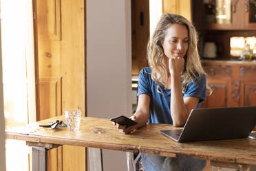 Weibliche Freiberuflerin mit Hand am Kinn bei der Arbeit am Laptop im Home Office - SBOF02660