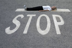 Frau in Freizeitkleidung liegt auf der Straße am STOP-Schild - PSTF00789