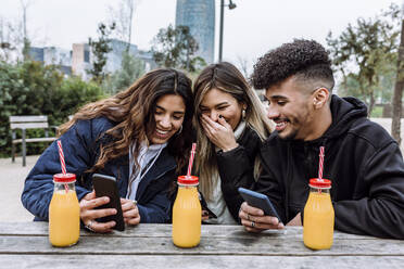 Fröhliche Freundinnen mit jungem Mann, der ein Smartphone benutzt - XLGF01115