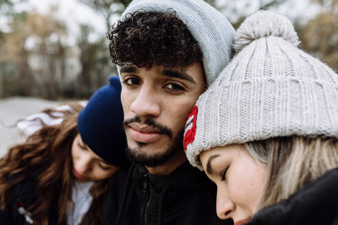 Female friends leaning on male friend shoulder at park - XLGF01122