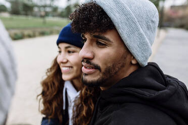 Young man in knit hat with female friends looking away at park - XLGF01124