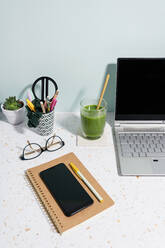 Laptop, gesunder grüner Saft, Buch, Mobiltelefon und Sukkulente über dem Schreibtisch zu Hause - GEMF04614