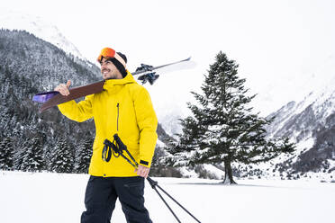 Junger Mann mit Ski, der wegschaut, während er durch ein verschneites Tal läuft - DAMF00680