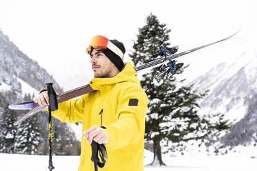 Nachdenklicher Mann mit Ski, der auf einem verschneiten Tal steht und wegschaut - DAMF00682