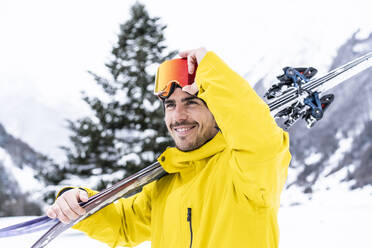 Lächelnder Mann mit Ski, der auf einem verschneiten Tal steht und wegschaut - DAMF00689