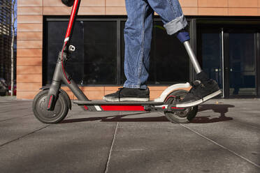 Young disabled man with prosthetic leg standing on electric push scooter - VEGF03756