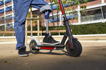 Behinderter Mann mit Beinprothese steht auf einem elektrischen Roller auf einem Spielplatz - VEGF03768