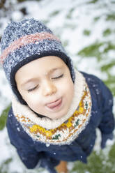 Nettes Mädchen mit geschlossenen Augen streckt im Winter die Zunge heraus - IFRF00368