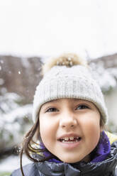 Niedliches lächelndes Mädchen mit Strickmütze bei Schneefall - IFRF00369