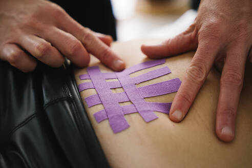 Krankenschwester klebt lila elastisches therapeutisches Band auf den Bauch einer Frau - MPPF01495
