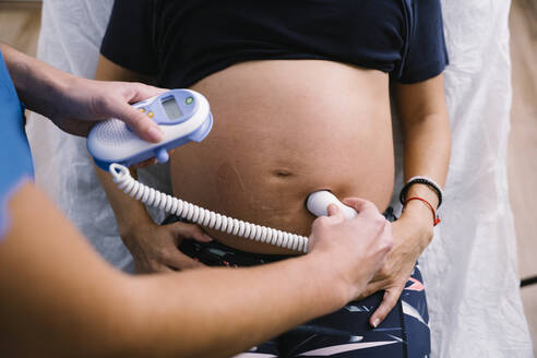 Female nurse examining pregnant woman abdomen by ultrasound baby heartbeat monitor - MPPF01501