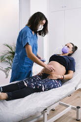 Midwife in protective face mask examining pregnant woman during COVID-19 - MPPF01502