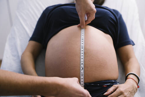 Female nurse measuring pregnant woman abdomen with measuring tape - MPPF01505