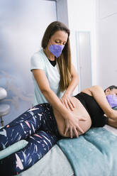 Midwife in protective face mask examining pregnant patient while exercising at hospital - MPPF01506