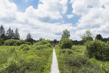 Man walking on boardwalk in High Fens Nature Park against cloudy sky - GWF06882