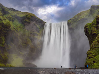 Reisende am Skogafoss-Wasserfall vor bewölktem Himmel, Island - LAF02663