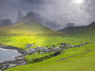 Grüne Landschaft und Dorf am Meer gegen bewölkten Himmel, Island - LAF02665