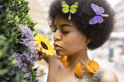 Junge Afro-Frau riecht an einer Blume im Freien - JCCMF01155
