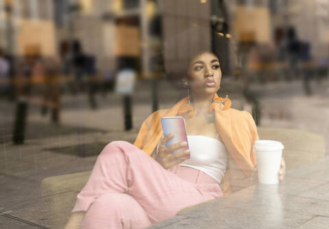 Afro woman with smart phone and coffee cup seen through glass at cafe stock photo