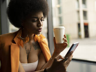 Female hipster text messaging on smart phone in cafe - JCCMF01166