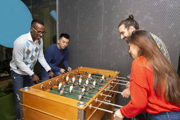 Cheerful young multiethnic people in casual clothes having fun and playing table football together - ADSF20600