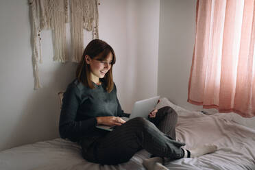 Blondes Mädchen sitzt auf dem Bett und arbeitet mit einem Laptop - ADSF20643