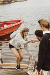 Man helping smiling female friend to climb on jetty - MASF21370