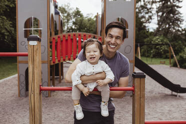 Smiling father and son leaning over monkey bar in park - MASF21395