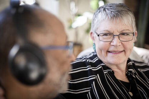 Lächelnde Frau sieht Mann mit Kopfhörern zu Hause an - MASF21415