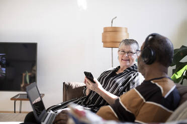 Älteres Paar mit Smartphone und Laptop auf dem Sofa im Wohnzimmer sitzend - MASF21421