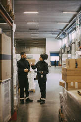 Male and female colleagues discussing while standing in logistics warehouse - MASF21439