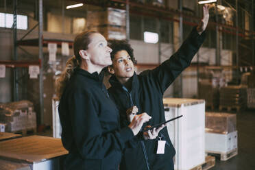 Businesswoman gesturing while discussing with female colleague at warehouse - MASF21448