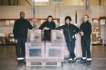 Porträt von lächelnden Arbeitern, die mit Boxcontainern in einem Logistiklager stehen - MASF21456