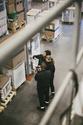 Weibliche und männliche Kollegen prüfen Pakete, während sie in einem Logistiklager stehen - MASF21458