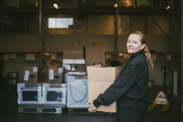 Mature businesswoman carrying box container in logistics warehouse - MASF21474
