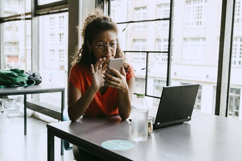 Geschäftsfrau, die ein Smartphone benutzt, während sie am Schreibtisch im Büro sitzt - MASF21502