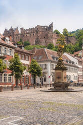 Germany, Baden-Wurttemberg, Heidelberg, Muttergottesbrunnen fountain on empty Kornmarkt square with Heidelberg Castle in background - TAMF02874