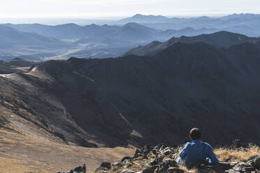 Männlicher Wanderer in den Bergen sitzend an einem sonnigen Tag - JAQF00240