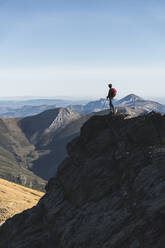 Male hiker exploring while standing on hill against clear sky - JAQF00242